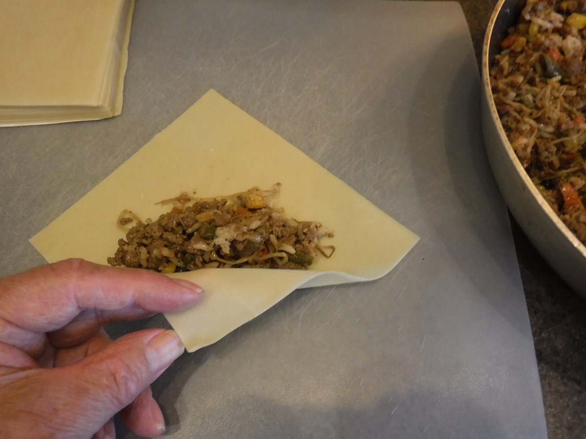 Click to enlarge - Place about 3 table spoons of the cooled mixture in the center of an egg roll skin and fold up bottom corner.